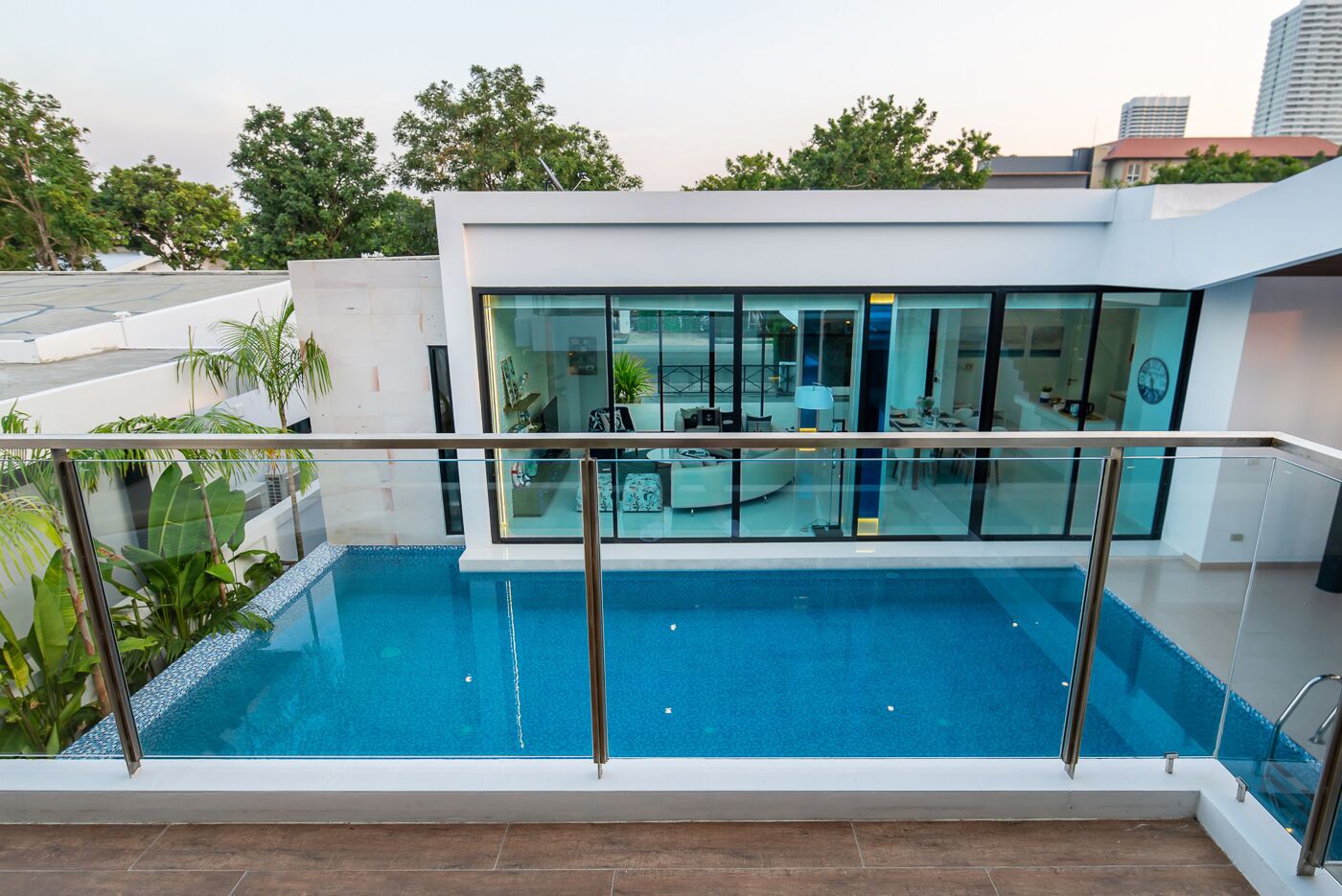 A modern building with a glass facade, a rooftop pool, and a balcony with a glass railing.