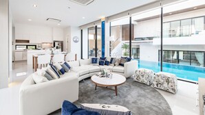 Uma sala de estar moderna com um sofá curvo, uma mesa de centro e vista para uma piscina.