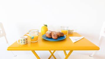 A yellow table with a plate of croissants, a lemon, and two glasses of orange juice.