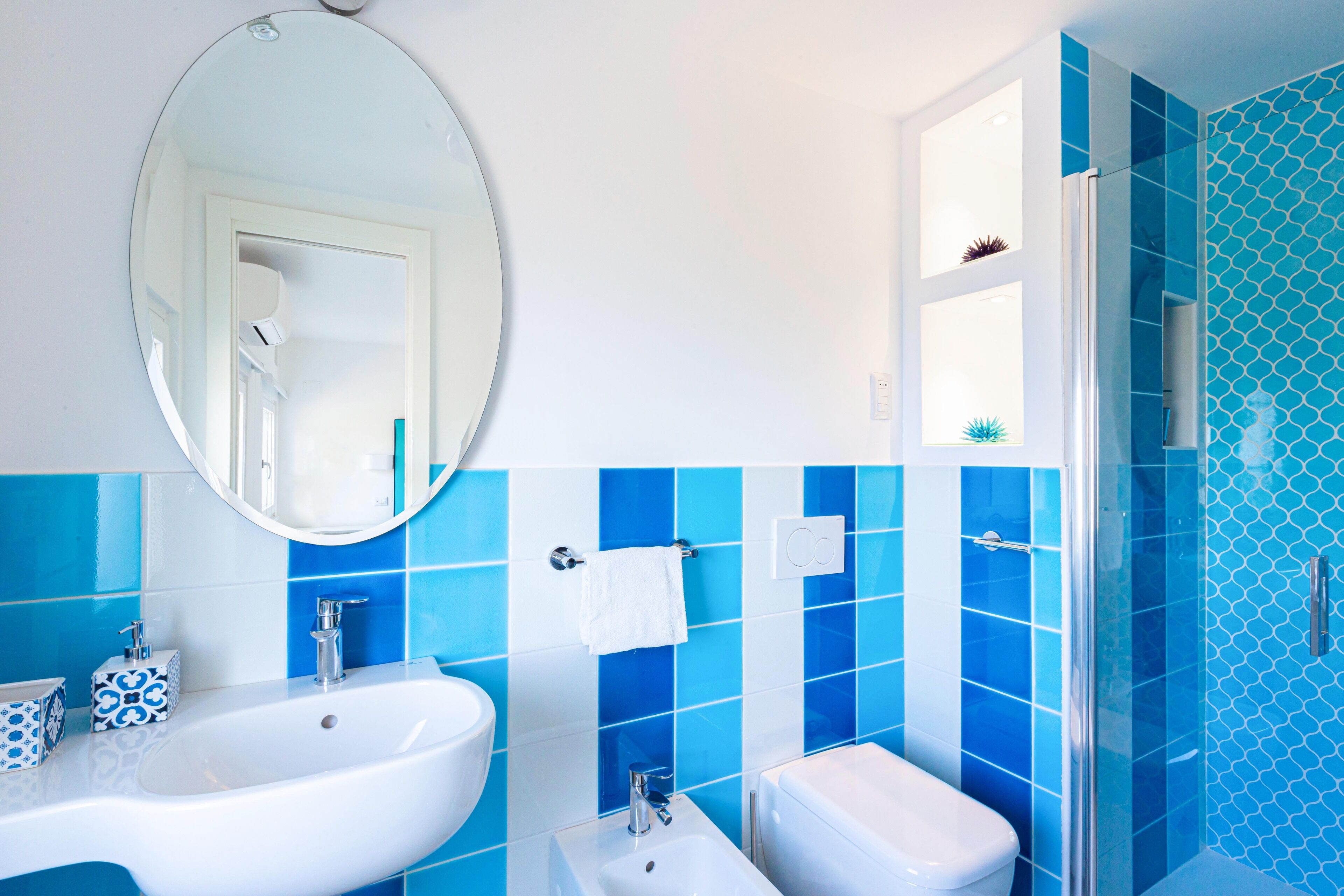 A bathroom with a white sink, a white toilet, and a shower with blue tiles.
