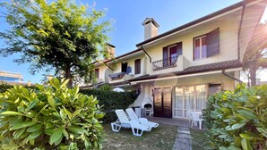 Ein zweistöckiges Haus mit einer Terrasse, auf der weiße Loungemöbel und ein Grill stehen.