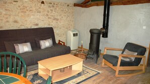 A cozy living room with a stone wall, a sofa, a wooden table, a chair, and a wood-burning stove. - Time for a break - the barn (Berbiguières)
