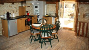 A rustic kitchen with wooden beams, stone walls, and a dining area with green chairs. - Time for a break - the barn (Berbiguières)