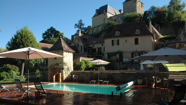 A pool area with lounge chairs and umbrellas, surrounded by stone buildings and a castle-like structure. - Time for a break - the barn (Berbiguières)