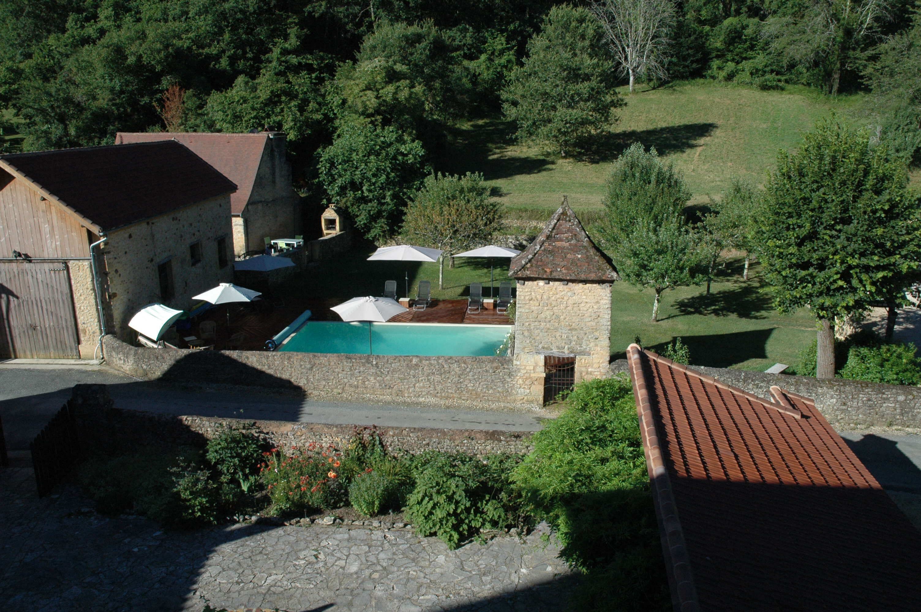 A stone building with a swimming pool, surrounded by greenery and a hilly landscape.