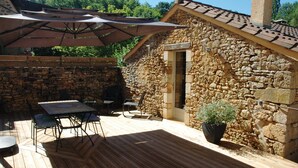 A stone building with a wooden deck, a table, chairs, and a potted plant. - Time for a break - the barn (Berbiguières)