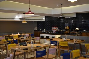 A modern restaurant with multiple dining tables and chairs, a black tiled backsplash, and overhead pendant lighting. - Ginger Vishakhapatnam Gajuwaka (Visakhapatnam)