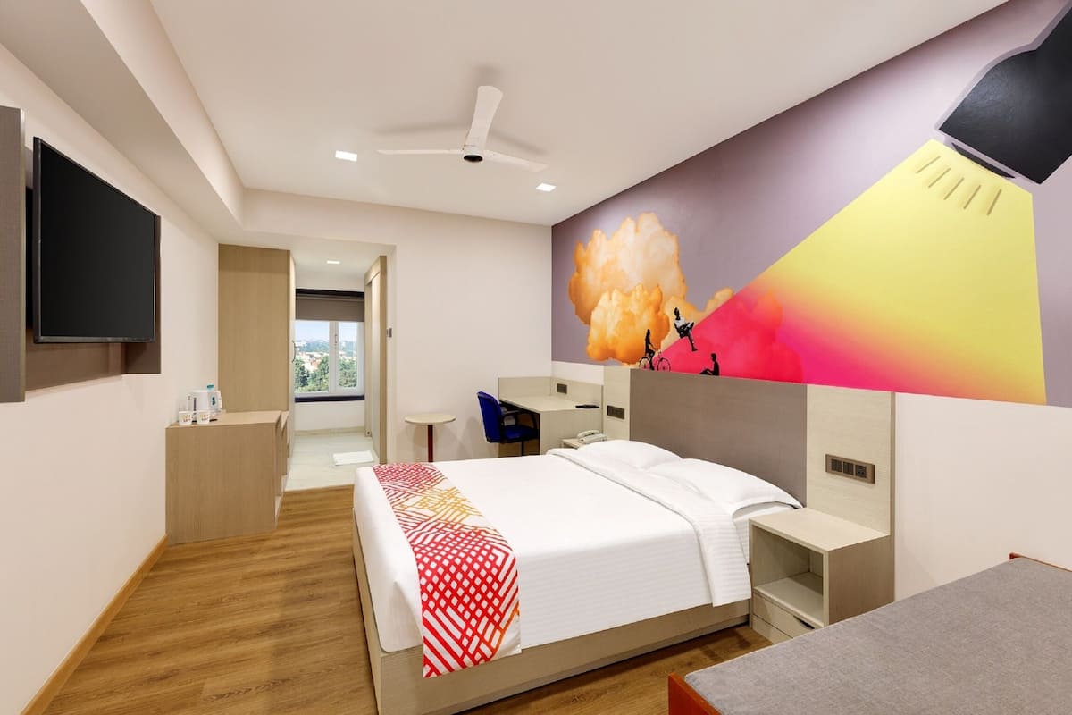Quarto de hotel moderno com cama, mesa de cabeceira e escrivaninha. Uma janela ampla oferece vista para o exterior.