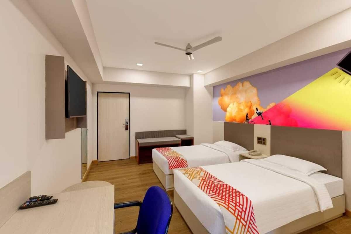 Quarto de hotel com duas camas, uma escrivaninha, uma cadeira, uma televisão e um ventilador de teto.
