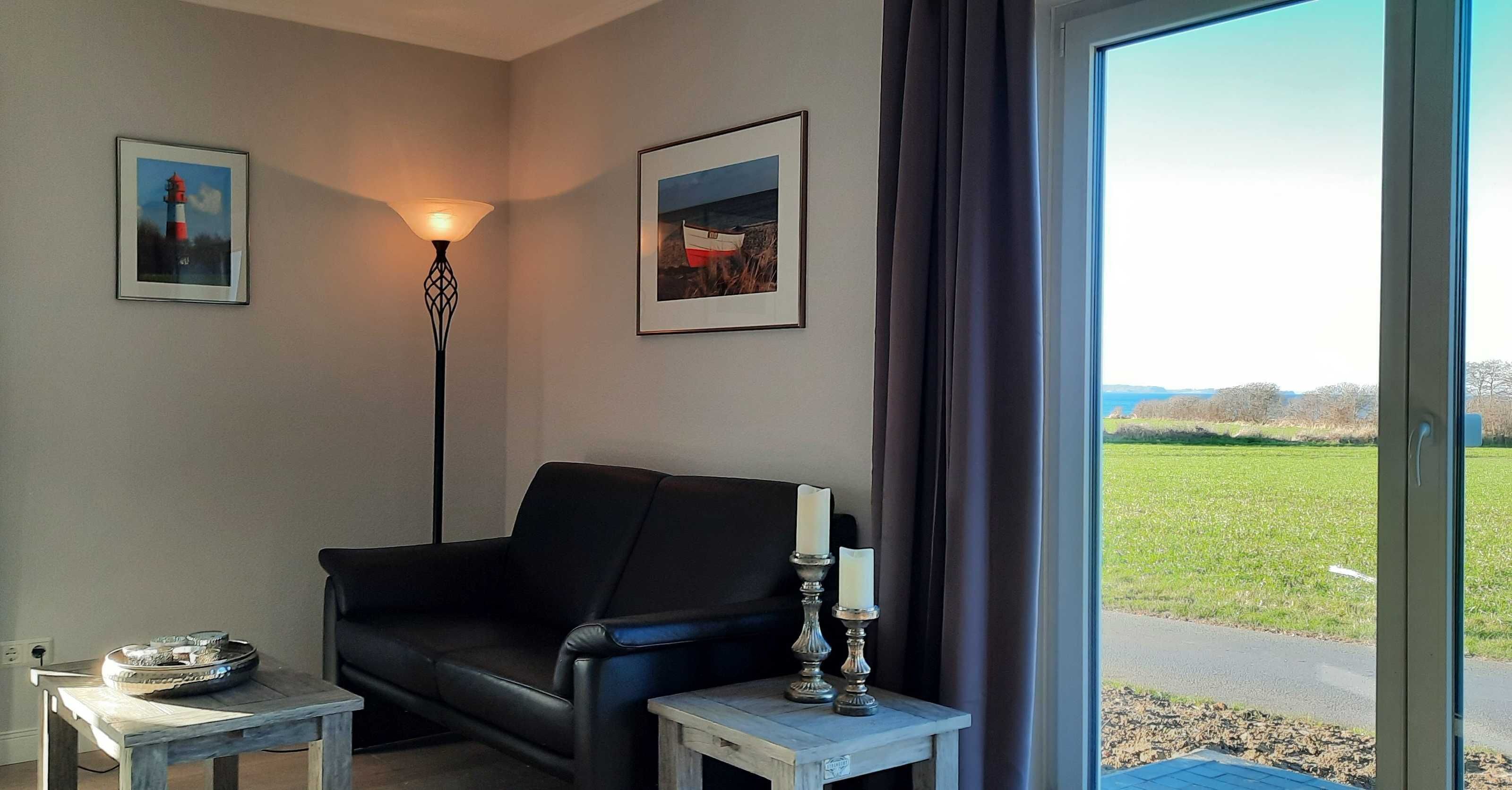 A living room with a black leather sofa, a small table with a candle, and two framed pictures on the wall.