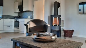 A modern kitchen with white cabinets, a black chair, a wood-burning stove, and a TV mounted on the wall.