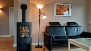 Un salon avec un poêle à bois noir, un canapé en cuir noir, une lampe sur pied et une œuvre d’art encadrée accrochée au mur.