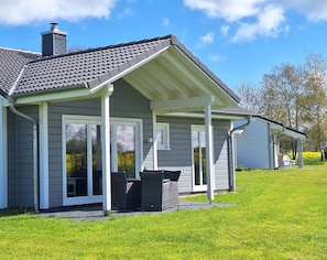 Une maison avec un porche couvert, une cheminée et une pelouse.