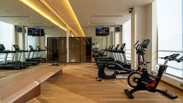A gym with exercise equipment, a long bench, and large windows.