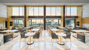 A spacious restaurant with high ceilings, large windows, and a variety of seating options including tables and chairs. - Gateway Ahmedabad Sindhu Bhavan (Ahmedabad)