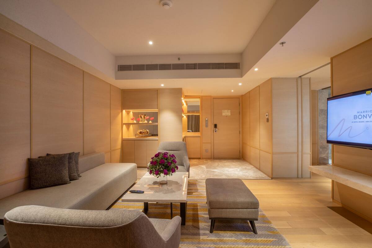 Ein modernes Hotelzimmer mit einer Couch, einem Sessel, einem Hocker und einem Flachbildfernseher.