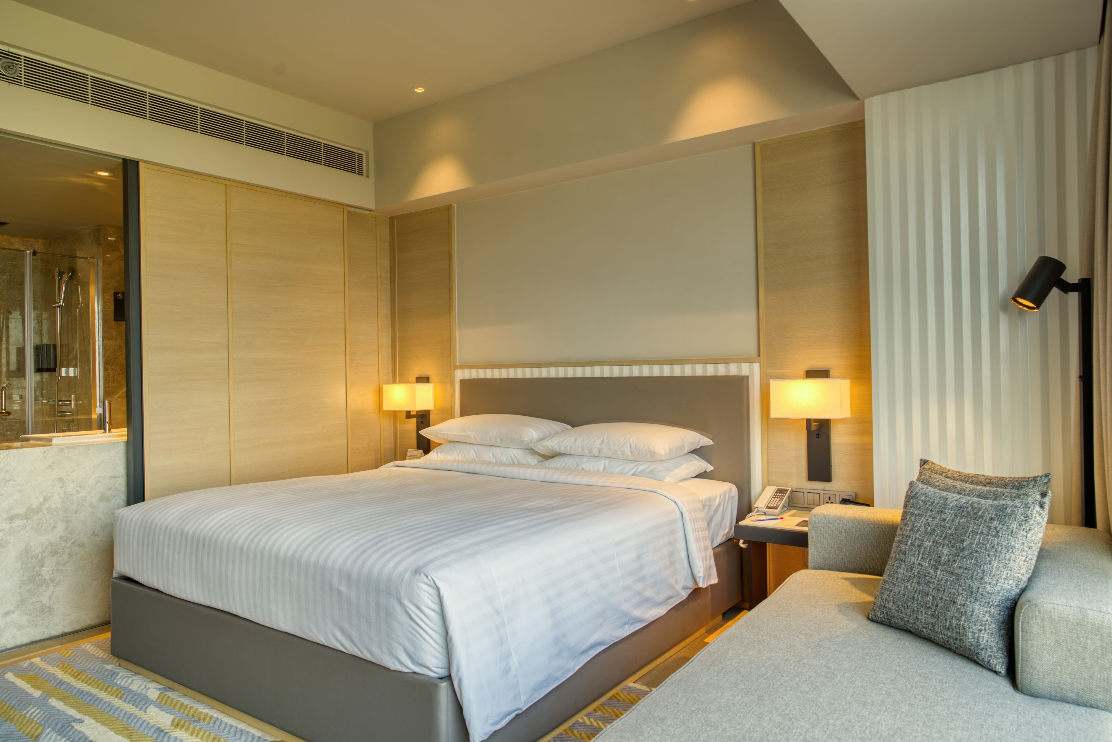 A modern hotel room with a large bed, bedside lamps, a nightstand, and a sofa.