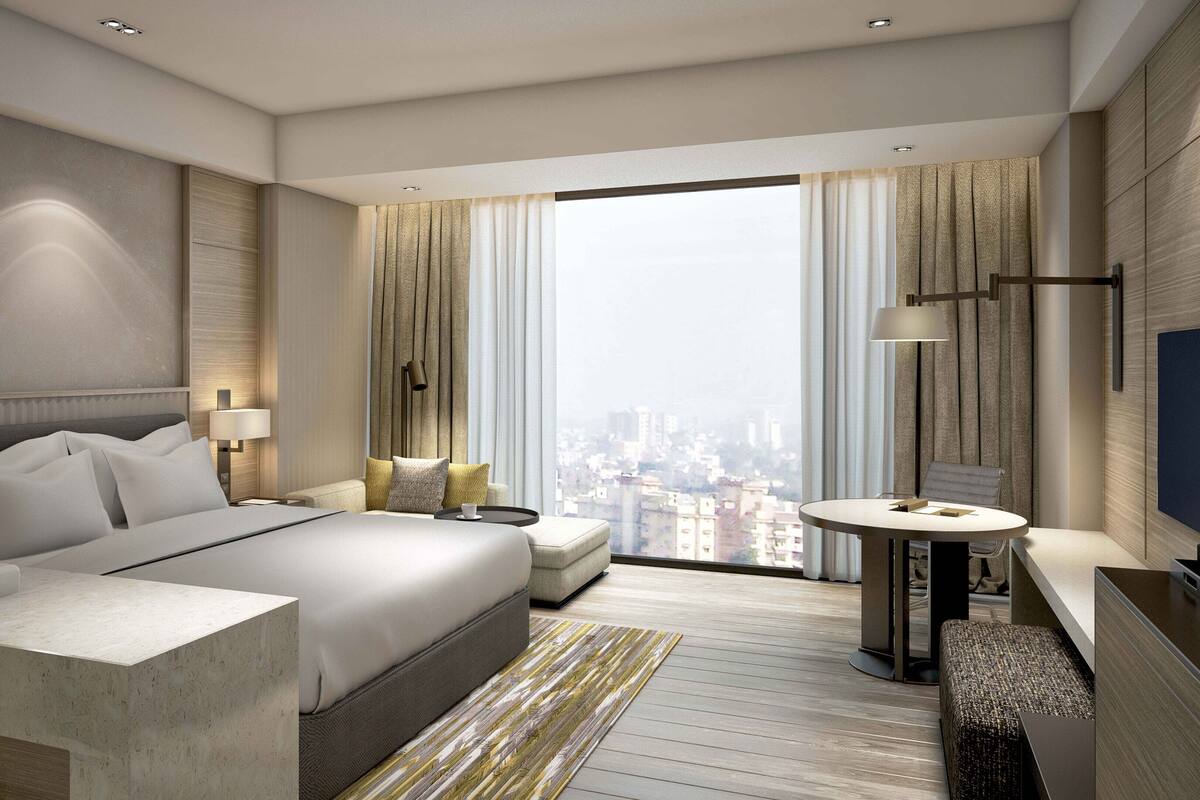 Ein modernes Hotelzimmer mit einem großen Bett, einer Sitzecke mit Tisch, einem Fernseher und Blick auf die Stadt.