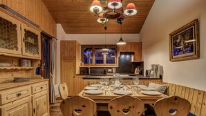 Un comedor de madera con una mesa dispuesta para cuatro comensales, sillas de madera con diseños de corazones, una araña y armarios de madera.