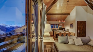 Un salón acogedor con un sofá, una mesa y vistas a una montaña nevada a través de una puerta de cristal.