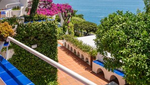 A balcony with a view of the sea, a white building with a blue awning, and a tree with pink flowers. - I giardini dell'Eden, Pool Amalfi Villa, jacuzzi, stunning view, garden, parking (Amalfi)