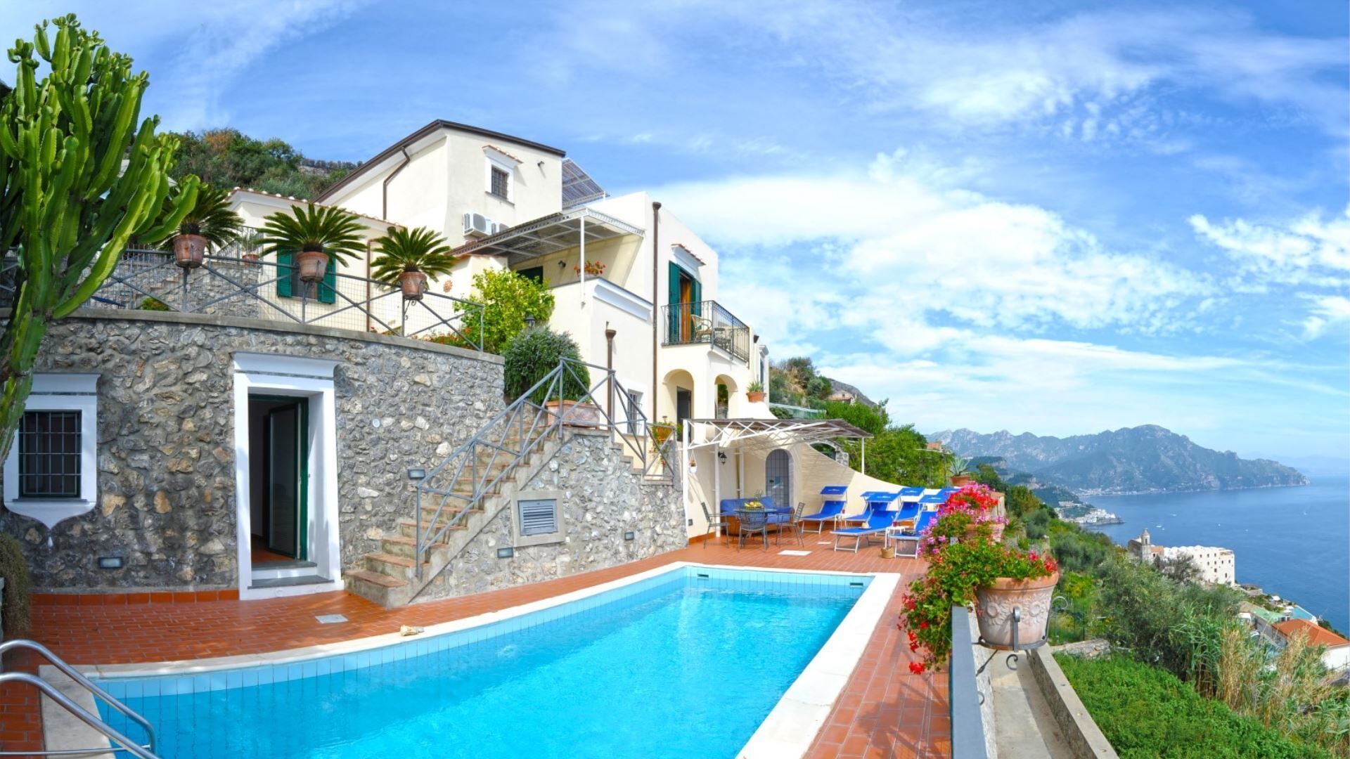 A poolside area with a stone building, a pool, and a view of the sea.