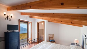 A bedroom with a bed, a dresser, a chair, a lamp, and a TV on a dresser. There are wooden beams on the ceiling and a door leading to a balcony with a view. - Mille e una notte Luxury Villa With Stunning Sea View and private pool (Conca dei Marini)