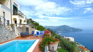 A poolside area with lounge chairs, a stone wall, and a view of the sea and mountains. - Mille e una notte Luxury Villa With Stunning Sea View and private pool (Conca dei Marini)