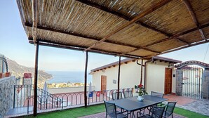A covered outdoor area with a table and chairs, a view of the sea, and a building with a door and gate. - Villa Belle, Panoramic Villa Near Ravello, Private Pool, garden, views, parking (Scala)