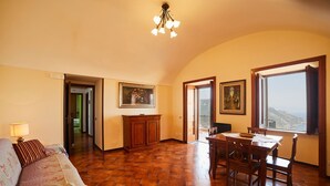 A spacious room with a tiled floor, a dining area with wooden furniture, a sofa with patterned cushions, and a painting on the wall. - Villa Belle, Panoramic Villa Near Ravello, Private Pool, garden, views, parking (Scala)