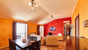 A spacious living area with a dining table, sofas, and a TV. There is a balcony with a view and a red accent wall. - Villa Belle, Panoramic Villa Near Ravello, Private Pool, garden, views, parking (Scala)