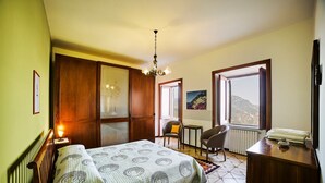 A bedroom with a bed, a desk, a chair, a window with a mountain view, and a chandelier. - Villa Belle, Panoramic Villa Near Ravello, Private Pool, garden, views, parking (Scala)
