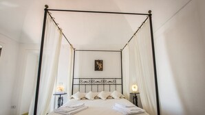 Una cama con dosel cubierta con sábanas y almohadas blancas, dos mesitas de noche con lámparas y un cuadro en la pared.