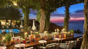 An outdoor dining area with a view of the sea, tables set with candles, and chairs with striped cushions. - La rosa, Luxury villa private pool Equipped With Conforts, wide garden,parking (Sorrento)