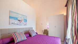 A bedroom with a bed, two pillows, a nightstand, a chair, a wardrobe, and a painting on the wall.