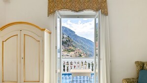 A room with a view of a mountainous landscape, a white door, a wicker bench, and a patterned sofa.
