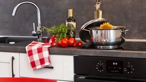A kitchen with a stainless steel pot on the stove, a bottle of olive oil, fresh tomatoes, and a red and white checkered cloth. - Nel Centro City Apartment (Rovinj)