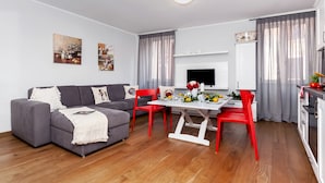 A modern living room with a grey sofa, red chairs, a dining table with flowers, and a TV. - Nel Centro City Apartment (Rovinj)