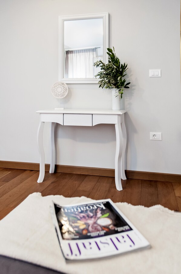A white desk with a mirror, a potted plant, and a magazine on a white rug.