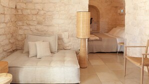 Um quarto com parede de pedra, uma cama, um sofá, um abajur e uma cadeira.