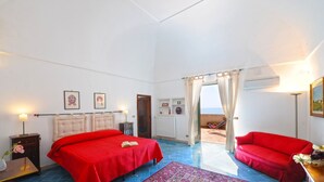 Ein Schlafzimmer mit zwei Betten, einem roten Sofa, Blick ins Freie und einem roten Teppich.