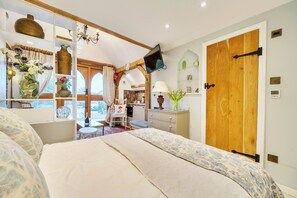 A bedroom with a bed, a TV, a wooden door, and a window with curtains. - Bramble Bank 'cartshed'-1 Bed Cottage-sleeps 2 (Henley-on-Thames)