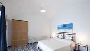 Quarto com cama, duas cadeiras, guarda-roupa e um quadro de uma praia.