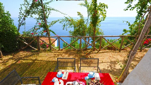 Un espace de restauration en plein air avec une table dressée pour deux personnes, offrant une vue panoramique sur la mer.