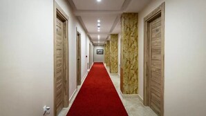 Un couloir d’hôtel avec un tapis rouge, des portes en bois et des murs en marbre.