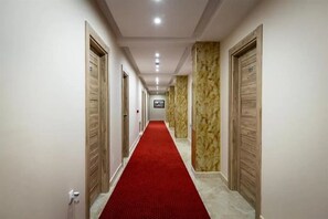 Un pasillo de hotel con alfombra roja, puertas de madera y paredes de mármol.