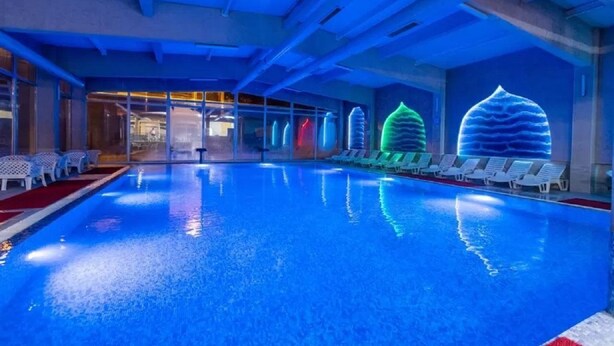 Une piscine dotée d’un éclairage bleu, de chaises longues et d’éléments décoratifs sur les murs.