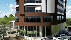 Un bâtiment moderne à plusieurs étages, doté d’une façade incurvée, de grandes fenêtres et d’un espace de stationnement où sont garées des voitures.