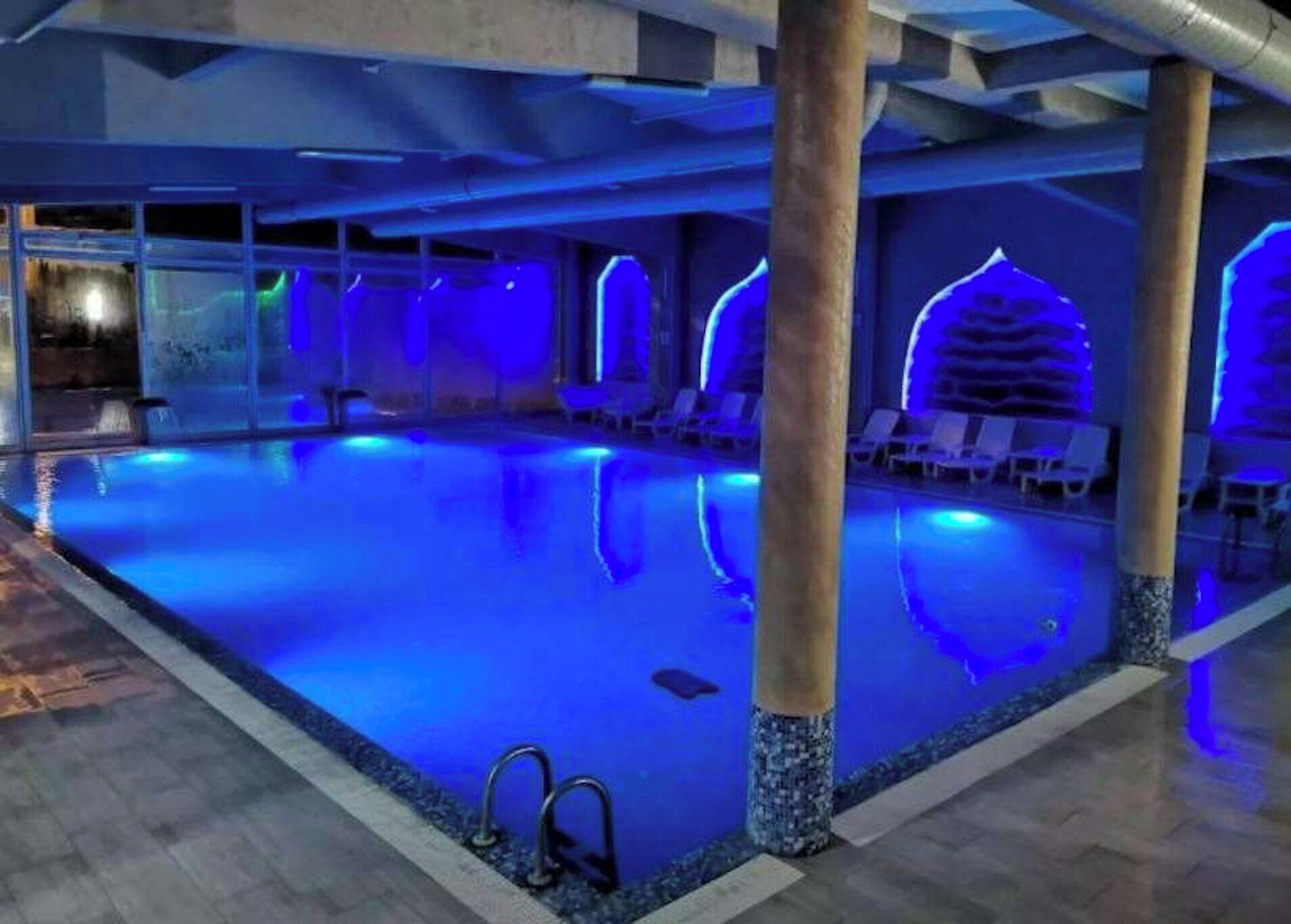 An indoor swimming pool with clear water, surrounded by lounge chairs and a tiled floor.