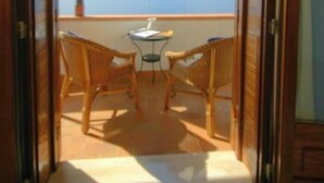 A room with a view of the ocean through a large window, a small table, and two wicker chairs.